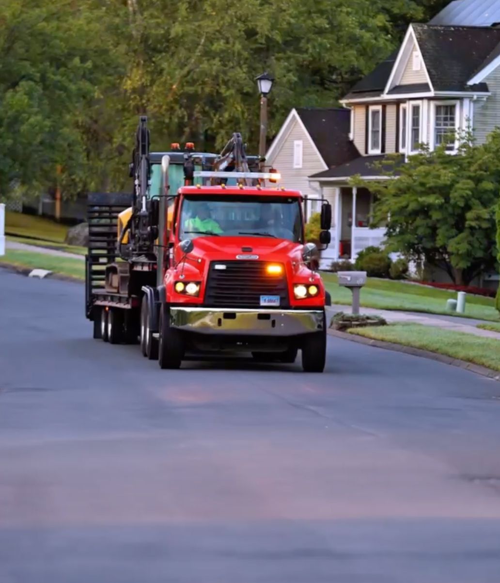 Red dump truck driving down a residential street with houses and trees in the background