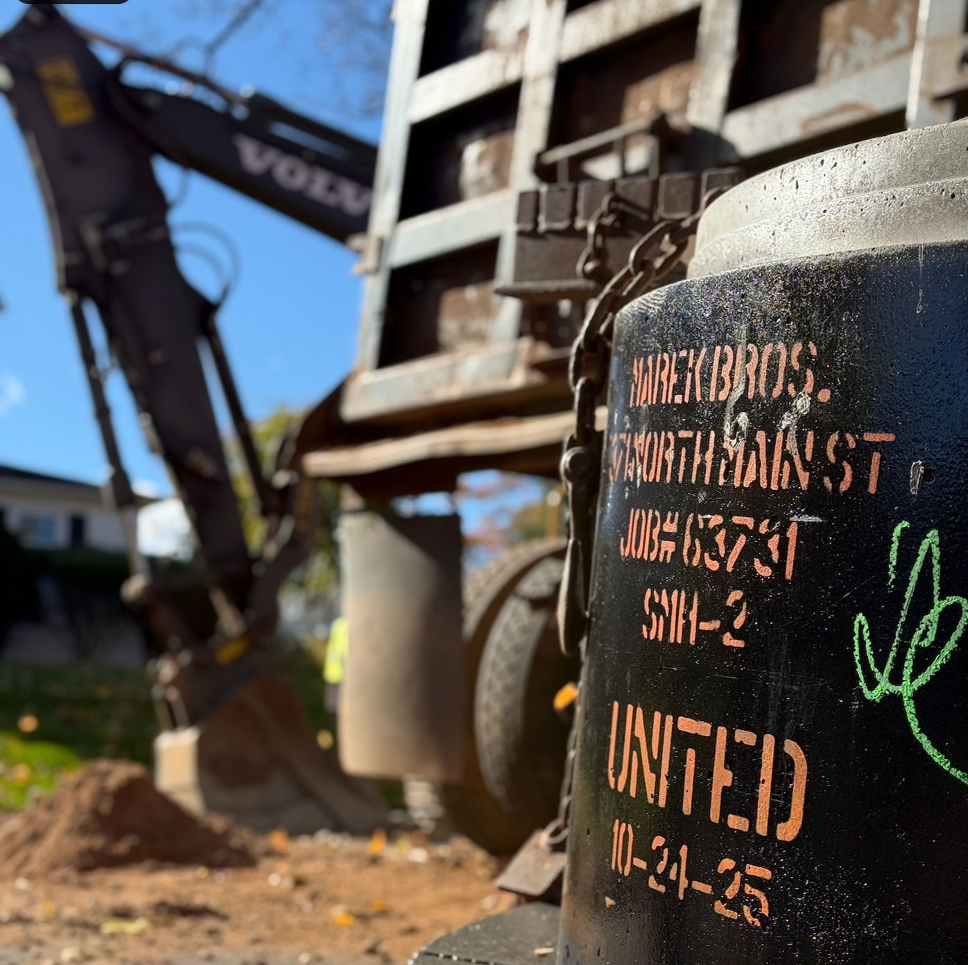 Spray-painted black construction bollard in rubble, with excavator and damaged building in background