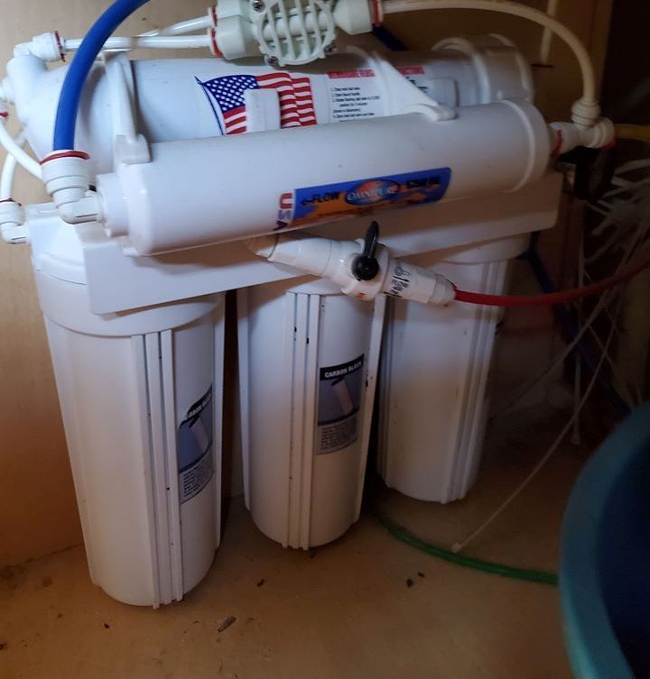 Reverse osmosis water filtration system with white filter housings and blue and red tubing.
