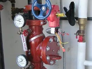 A red valve with a blue handle and two pressure gauges attached to it.