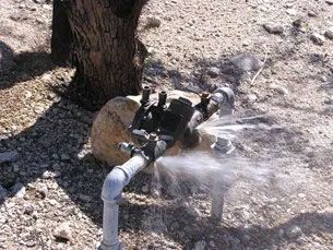 A water pump is spraying water from a pipe in the dirt.