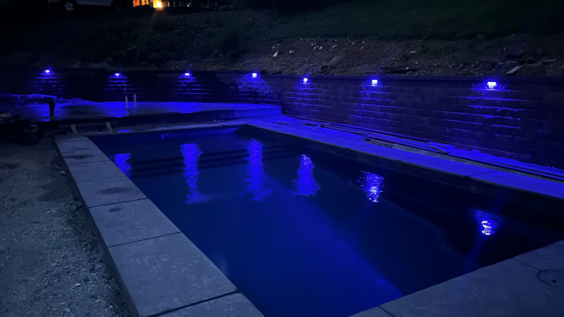A swimming pool is lit up with blue lights at night.