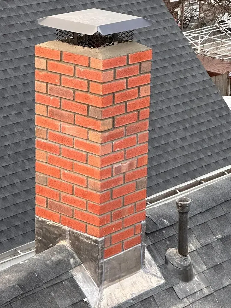 Red brick chimney with a metal cap on a gray shingled roof