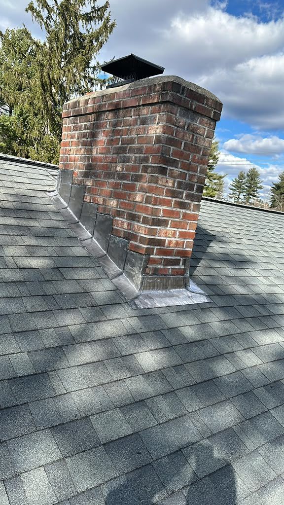Brick chimney on a gray shingled roof under a partly cloudy sky