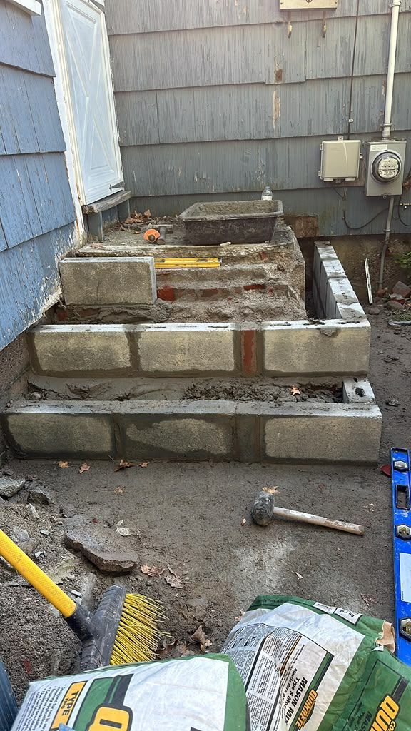 Partially built cinder block steps beside a house exterior, with tools and construction materials nearby