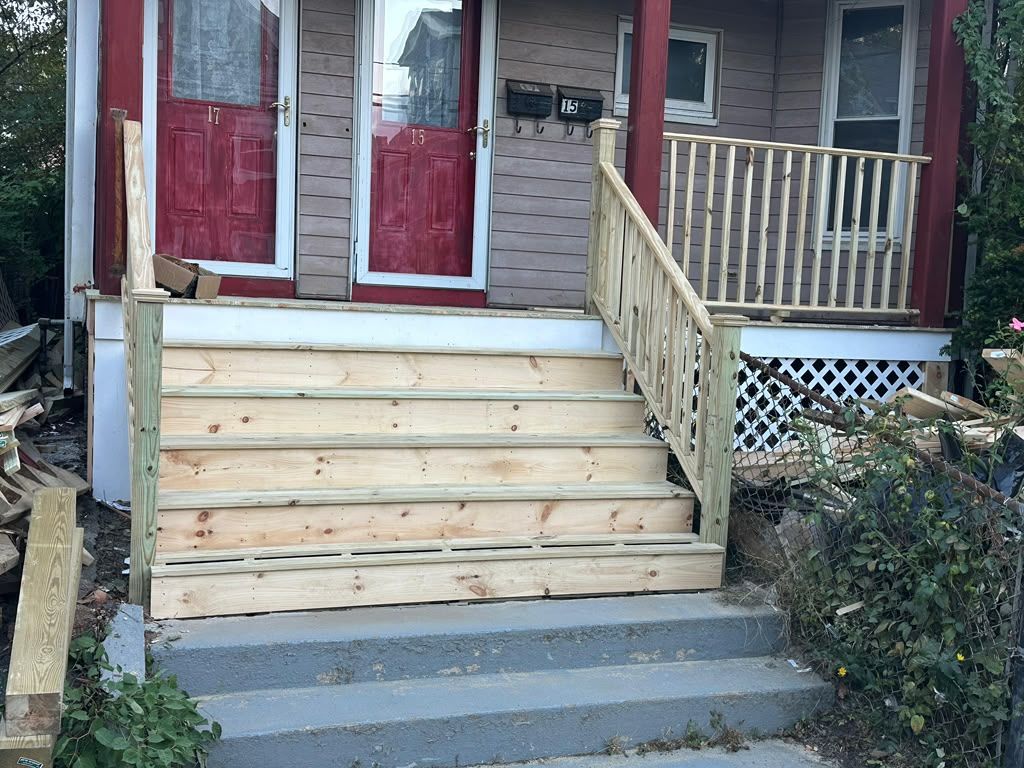 Front steps with a wooden ramp and railing leading to red double doors on a house porch