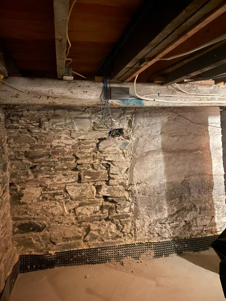 Exposed stone basement wall with wooden ceiling beams and dark floor under renovation