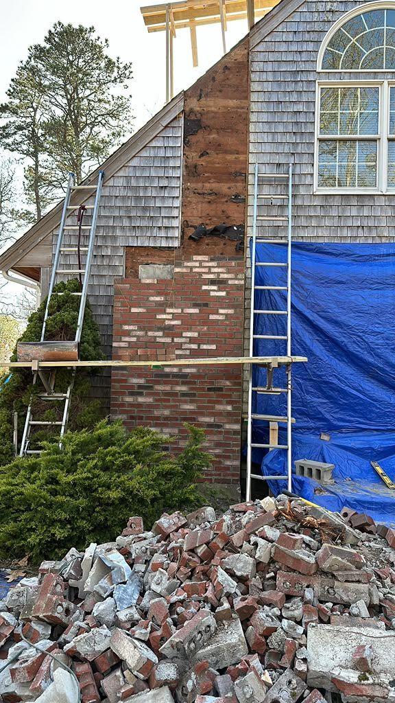House exterior under renovation with scaffolding, blue tarp, and pile of bricks in front