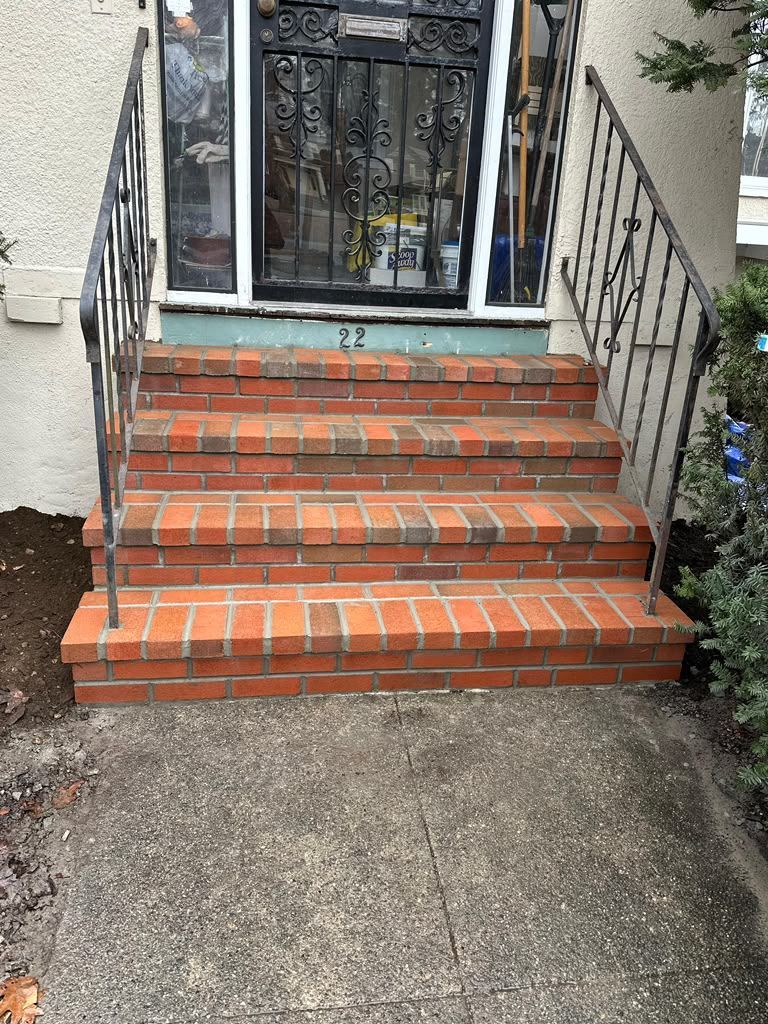Brick front steps leading to a dark metal security door with railings and cracked concrete walkway
