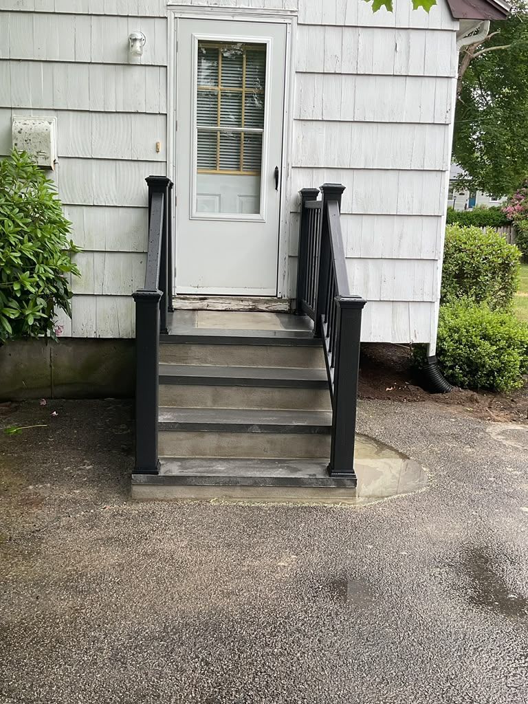 Front entrance with white door, short stairs, and black railings beside a light gray house.