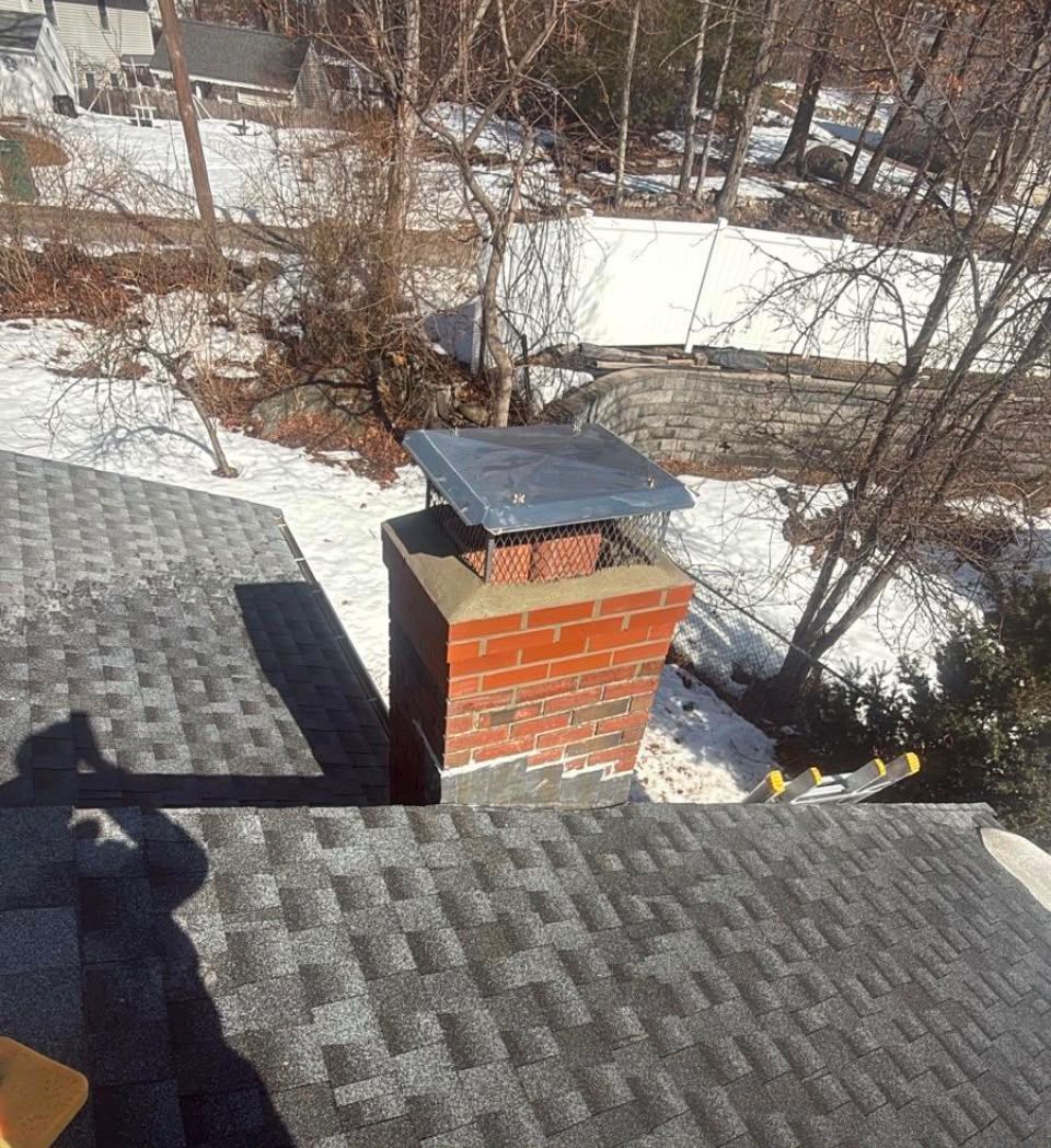 Snowy rooftop with gray shingles and a red brick chimney capped in metal.