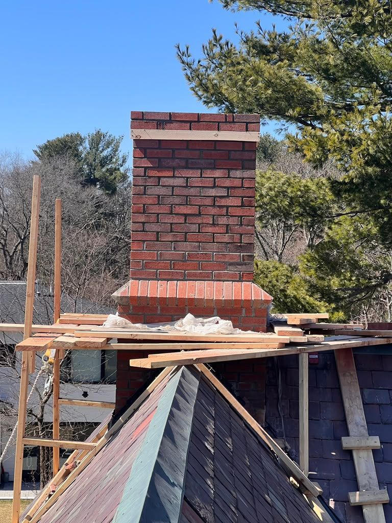 Brick chimney under construction on a rooftop with wooden scaffolding and trees in the background