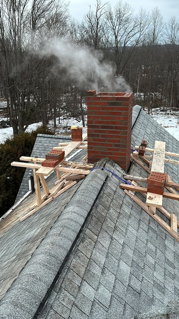 Roof under construction with brick chimney smoking, surrounded by wooden scaffolding and snowy trees