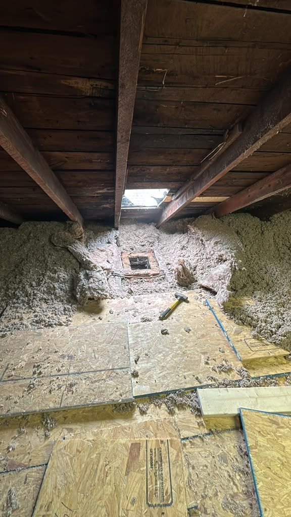 Attic interior with exposed wooden beams and insulation debris scattered on the floor