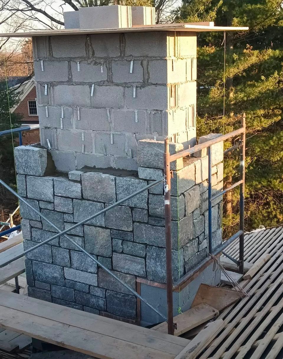 Stone chimney under repair with scaffolding and wooden planks on a rooftop