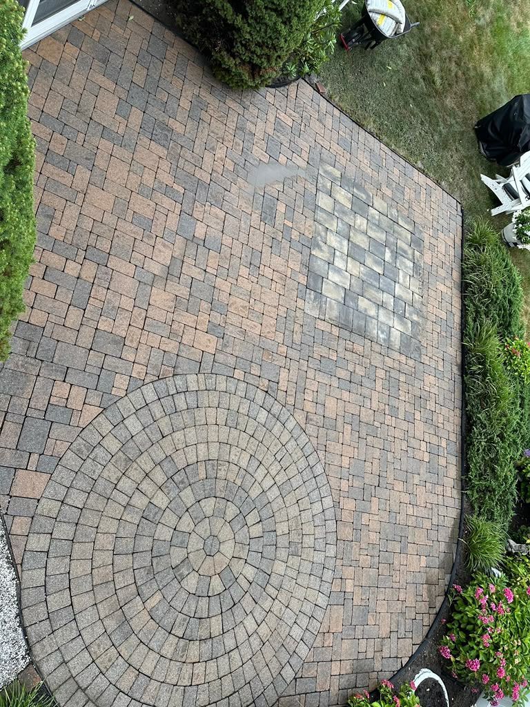 Stone patio with a circular brick pattern, bordered by grass and garden plants.