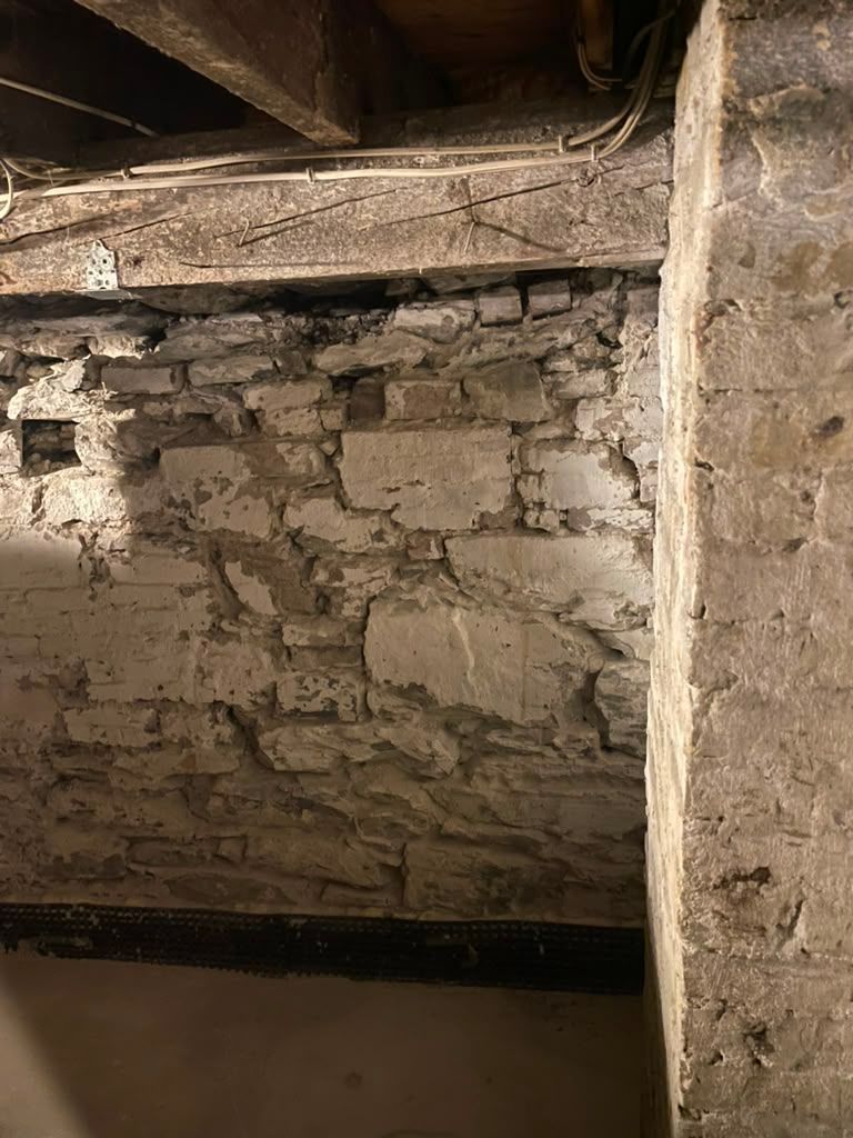 Old stone wall with rough plaster and wooden beams in a dim interior passage.