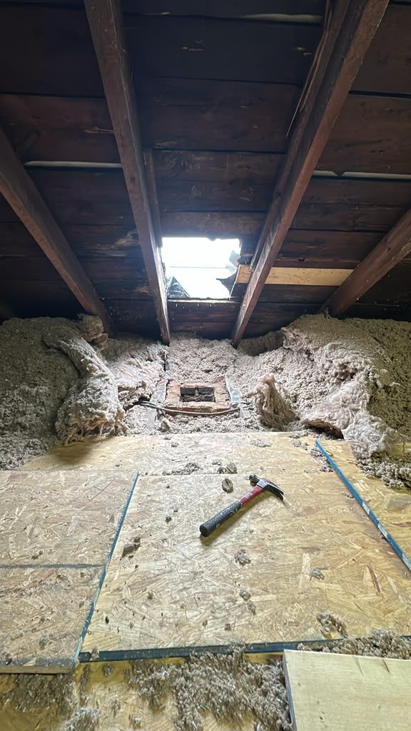 Exposed attic roof with daylight through a hole, damaged insulation, and a hammer on the floor