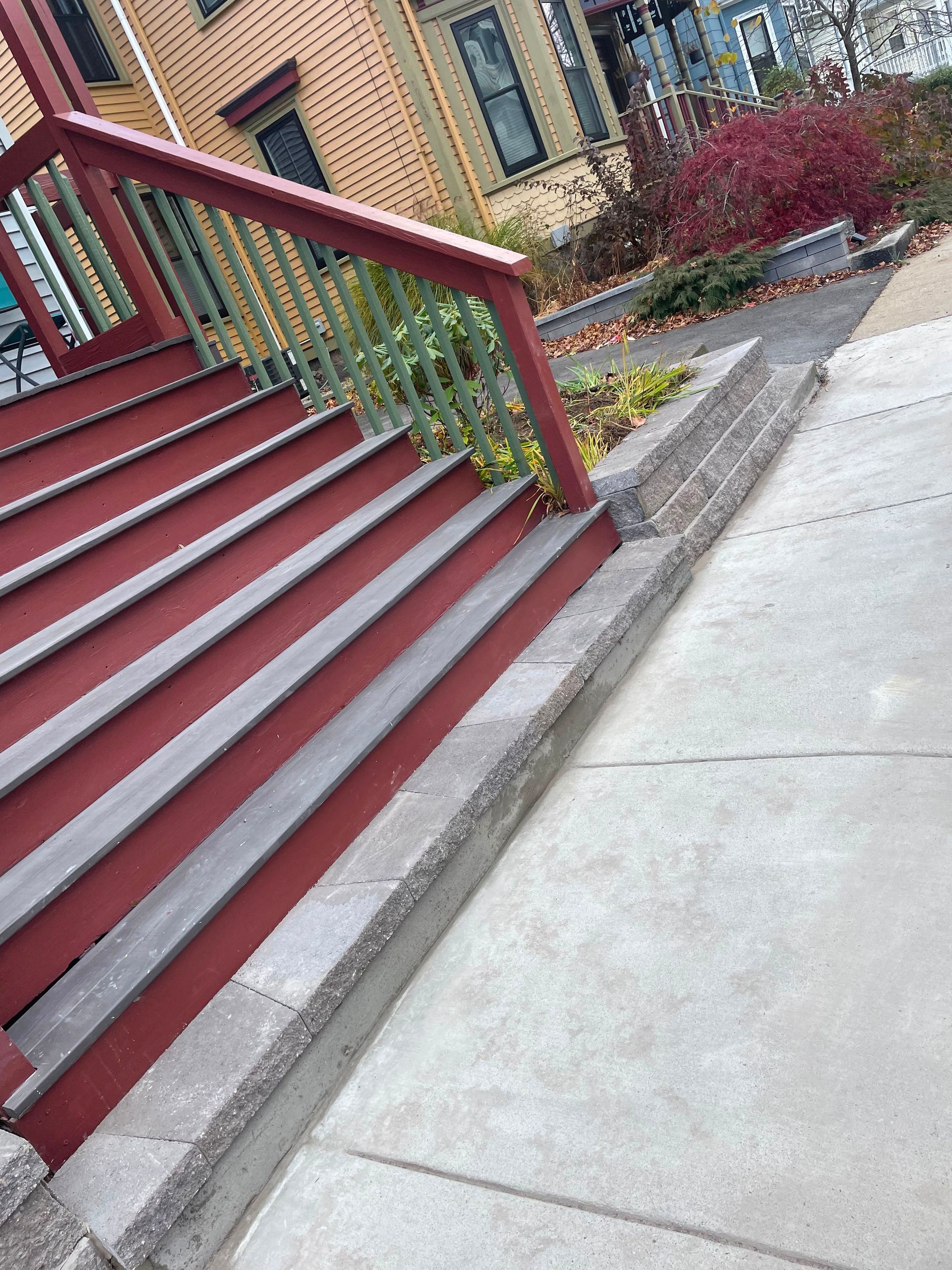Tilted view of red stairs with handrail beside a concrete sidewalk and building entrance.