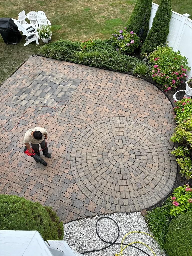 Person pressure washing a brick patio in a backyard.