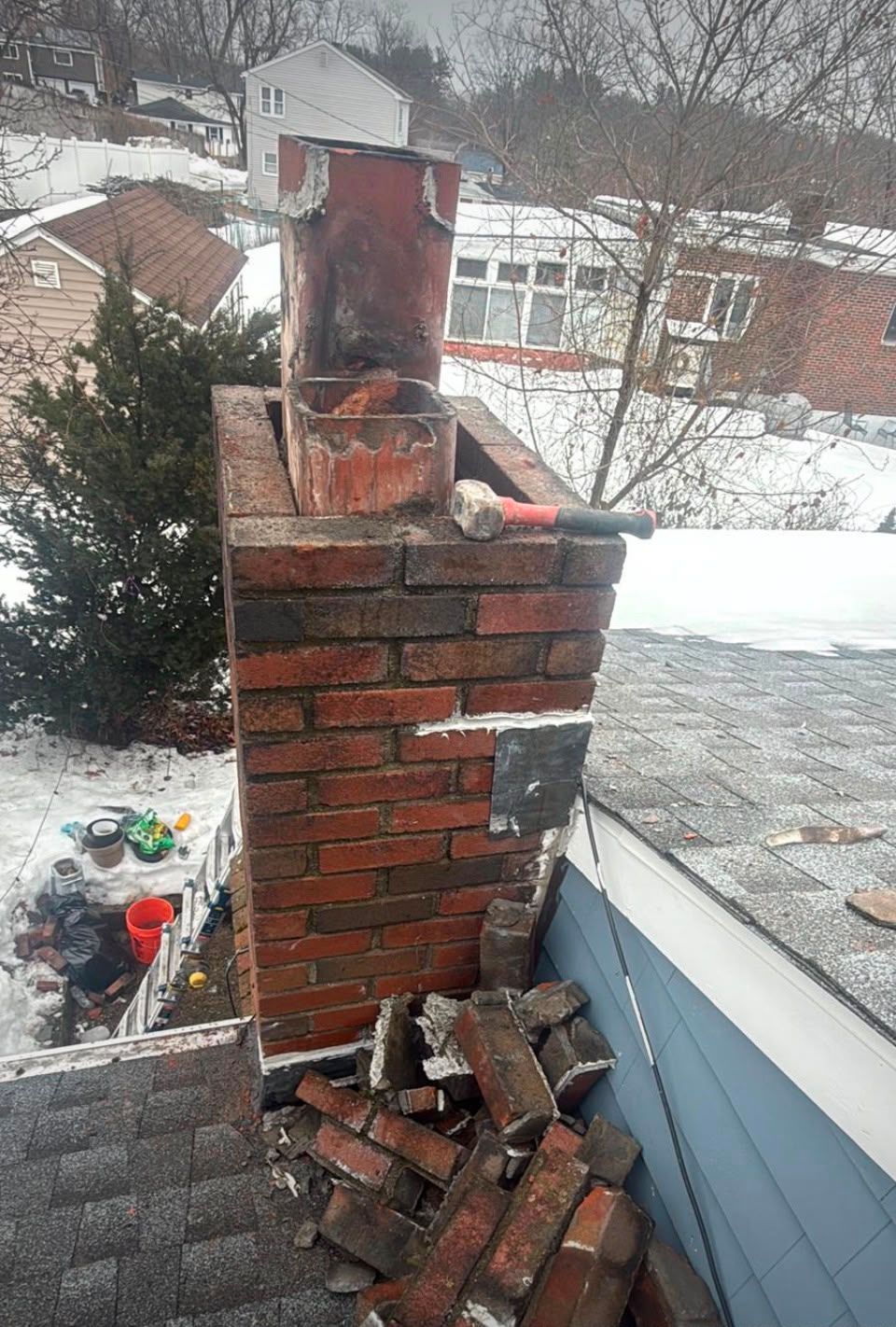 Damaged brick chimney with loose bricks and snow on a rooftop in winter