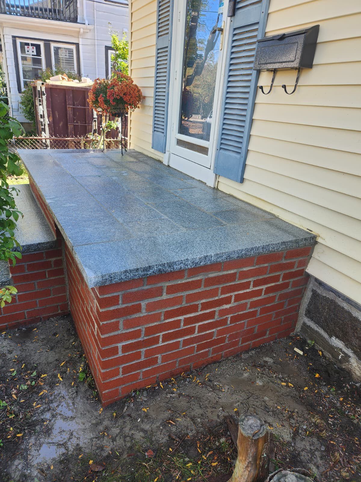 Small brick porch with a gray concrete top beside a house and front door.