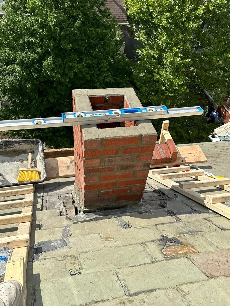 Brick chimney under construction on a rooftop, with wooden planks and tools around it.