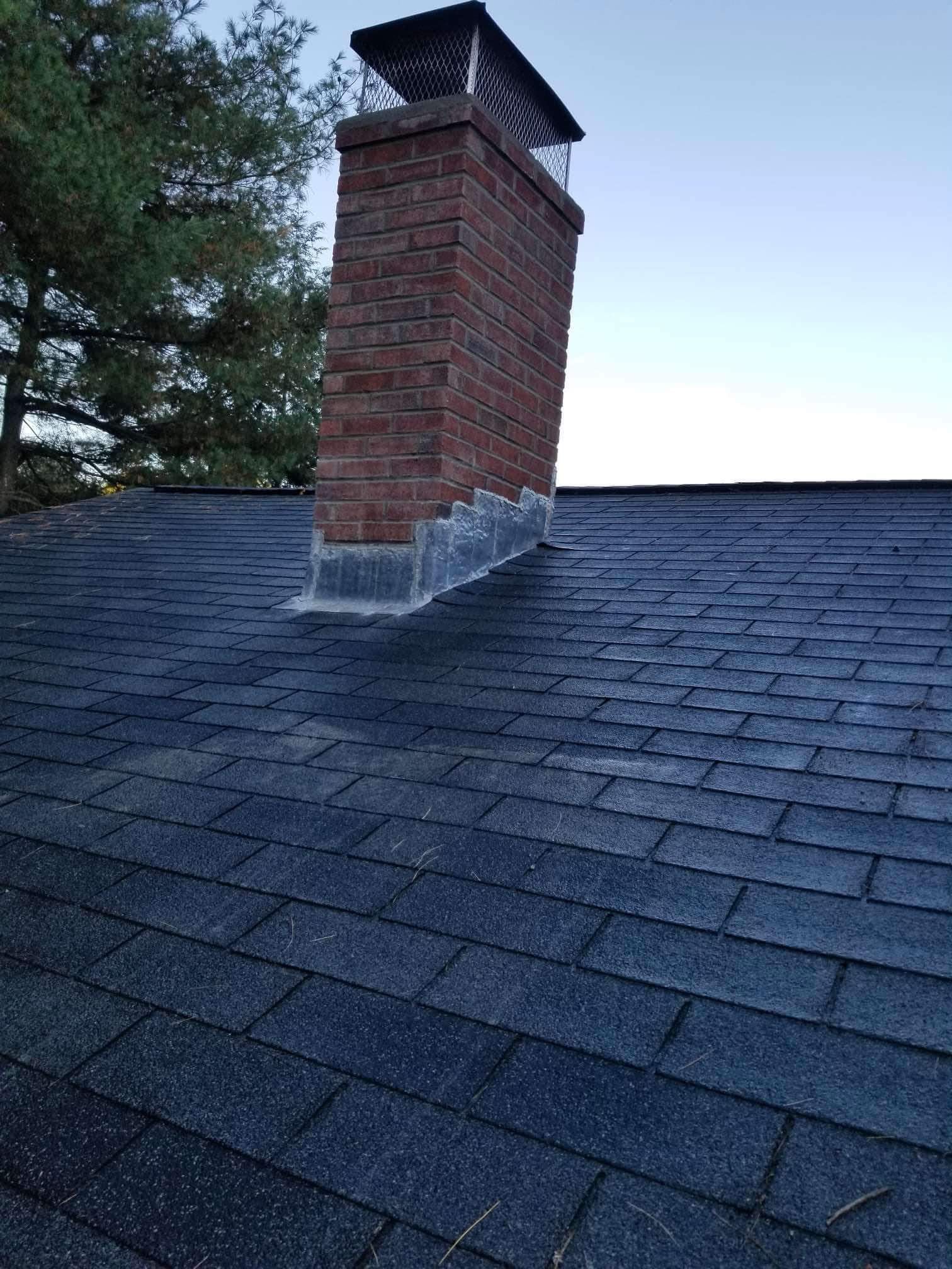 Dark shingled roof with a red brick chimney against a pale evening sky