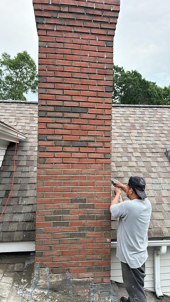 Worker repairing a red brick chimney on a shingled roof outdoors