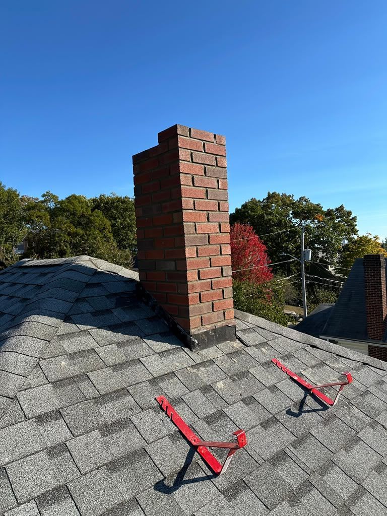 Roof with two red harness lanyards near a brick chimney under a clear blue sky