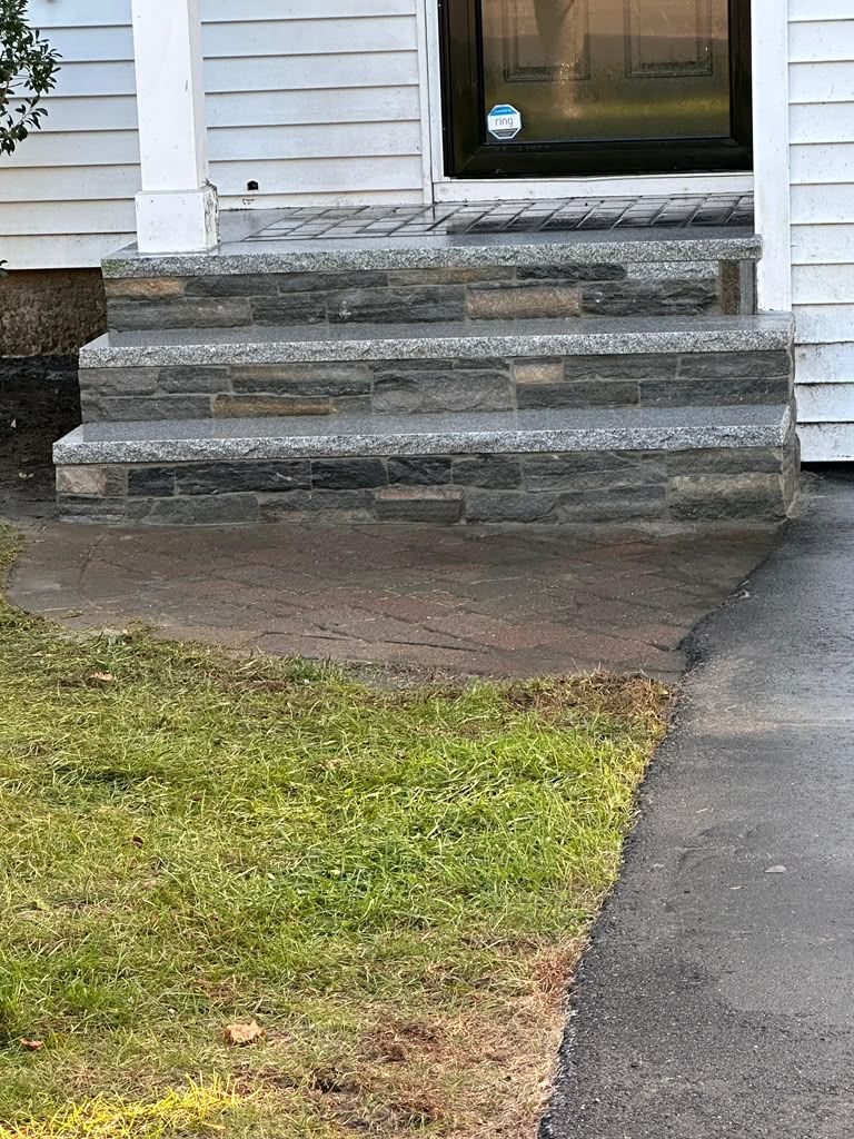 Stone front steps leading to a white house entrance beside a small lawn and walkway