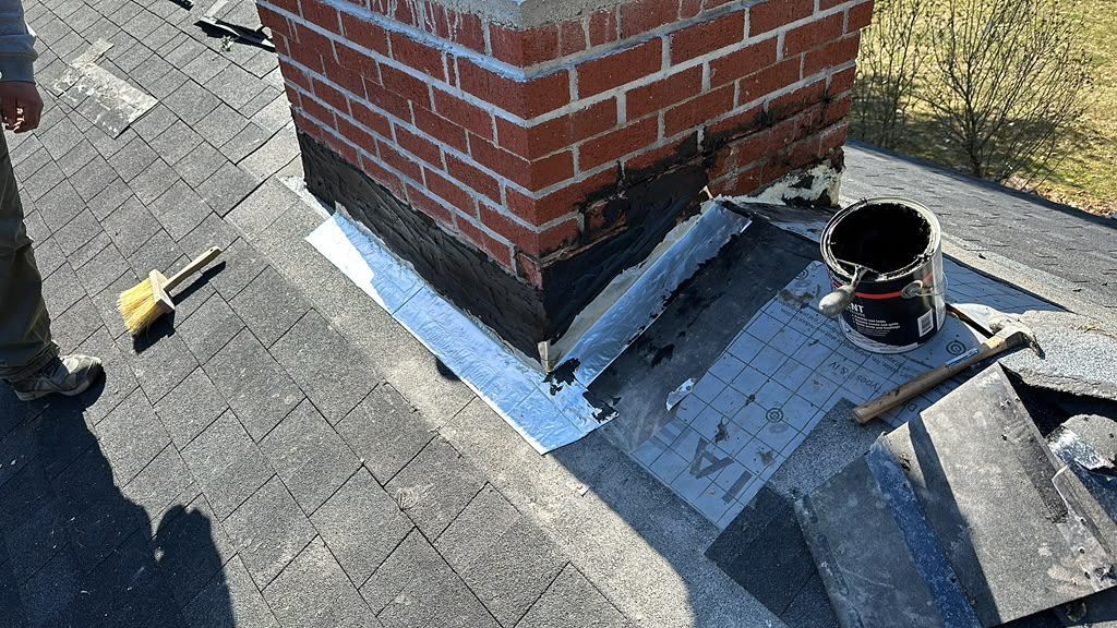Roof around brick chimney with flashing repair materials and tools on shingles