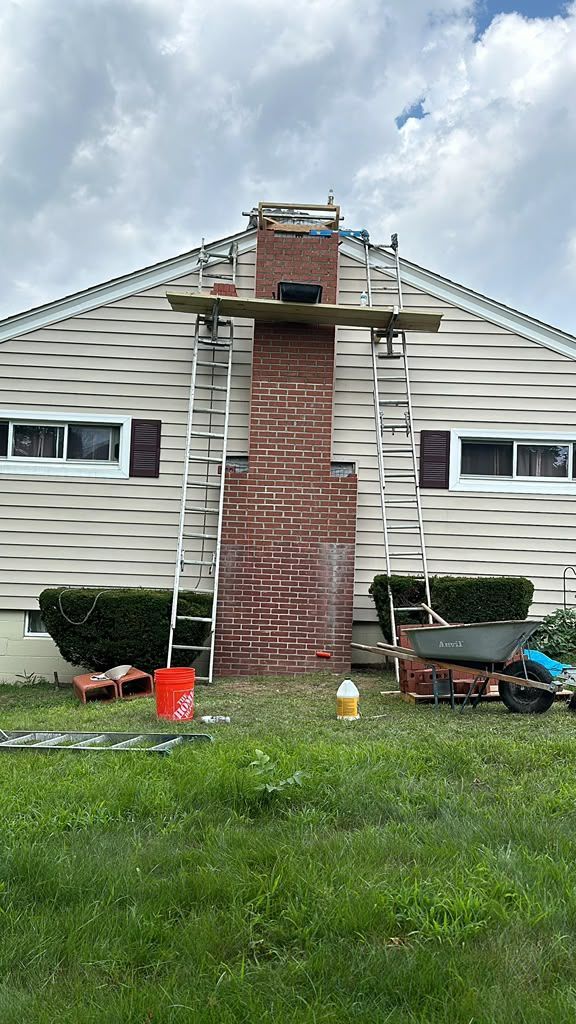House exterior with a brick chimney under repair, ladders on roof, and tools on the lawn