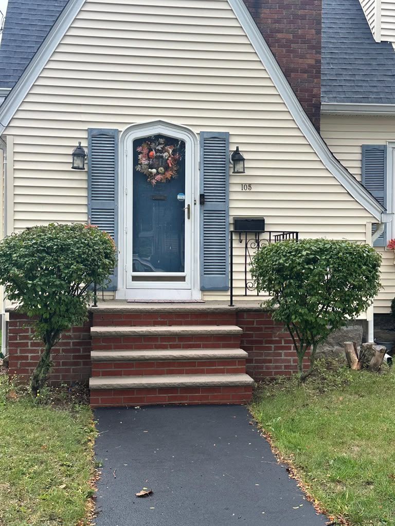 Front entrance of a house with blue door, brick steps, and trimmed bushes along a walkway.