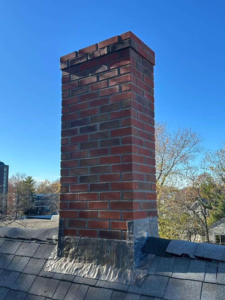 Red brick chimney on a roof with blue sky and trees in the background