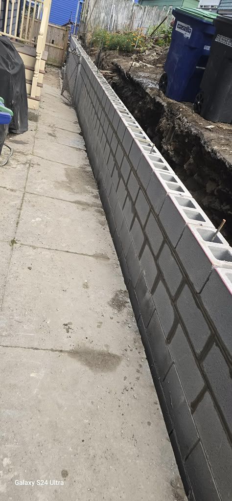 Narrow sidewalk beside a partially built cinder block wall along a dirt trench in an alley