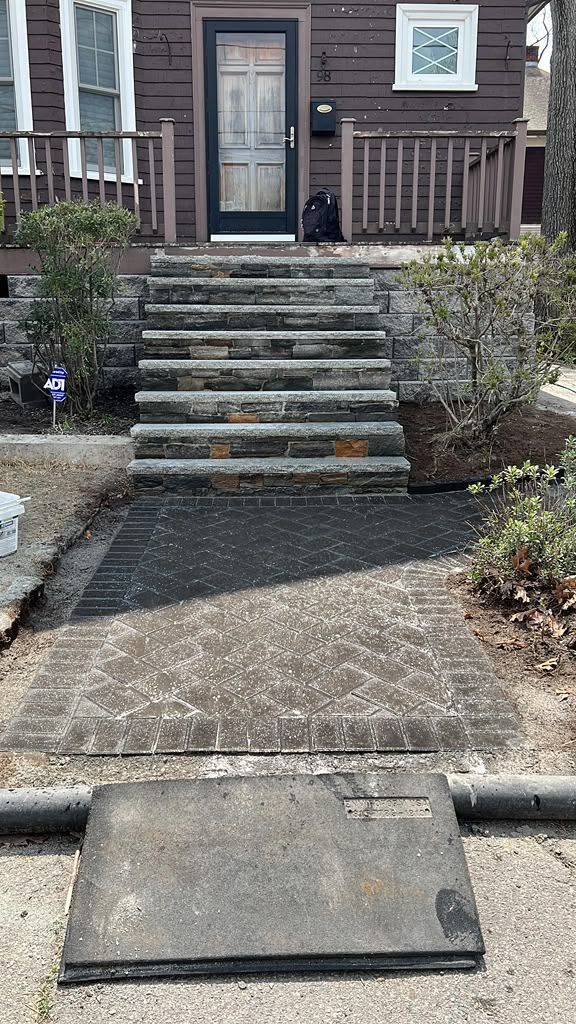 Front steps to a brown house with a black cat on the porch and a ramp leading up from the walkway