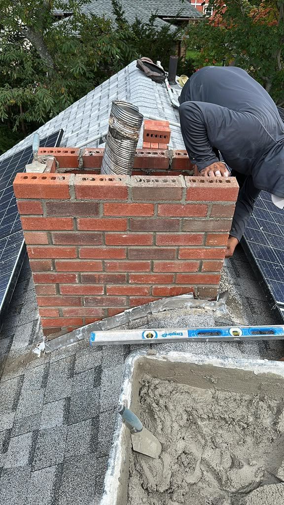 Brick chimney under construction on a roof, with a worker bending over beside it.