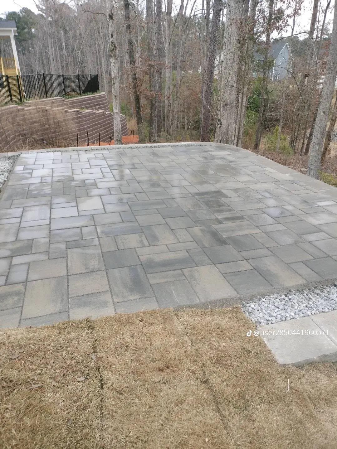 Stone patio in a backyard with a lawn, trees, and a wooded slope in the background.