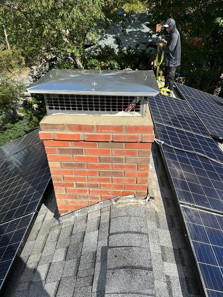 Worker on a rooftop beside a brick chimney, inspecting solar panels and equipment.