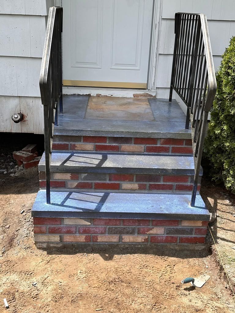 Front steps with brick risers, worn blue treads, and black railings leading to a white door