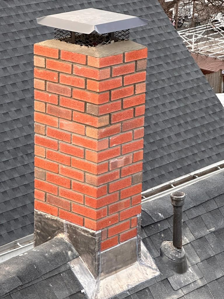 Red brick chimney with a metal cap on a gray shingled roof