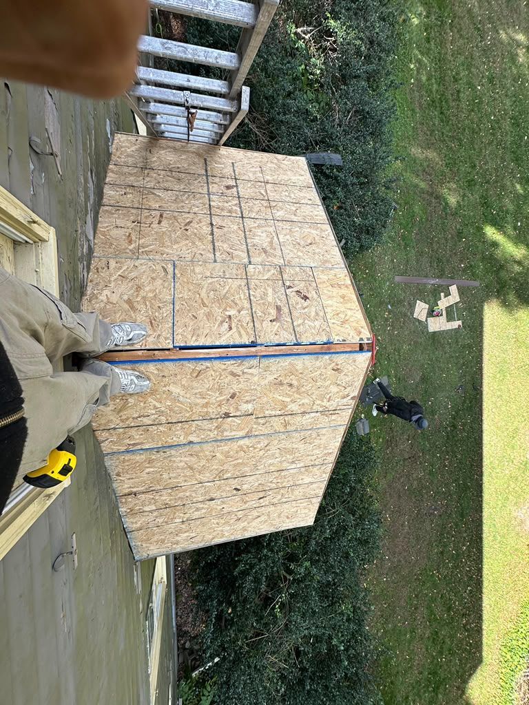 Wooden crate on a patio beside a ladder, with a person holding a yellow tool in the foreground.