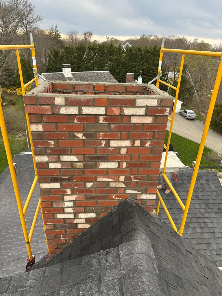 Brick chimney on a roof with yellow scaffolding on both sides and trees in the background