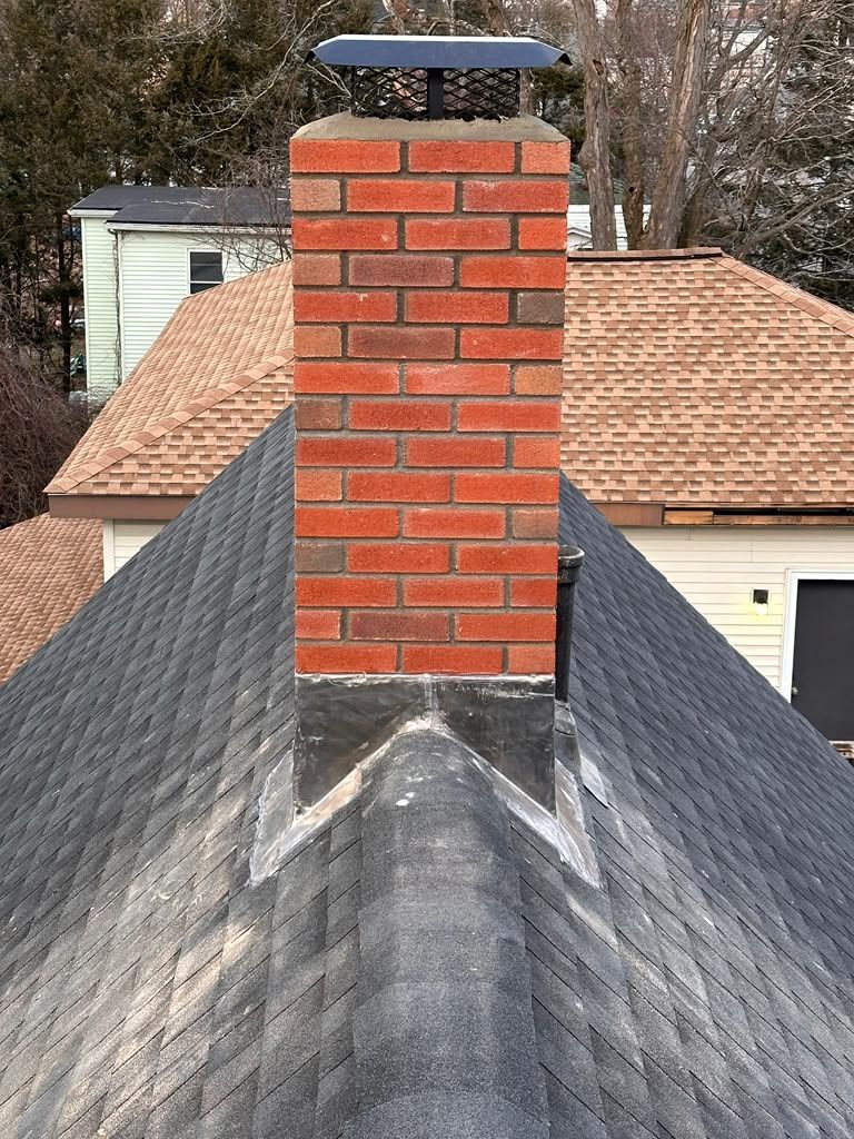 Brick chimney on a shingled roof with a metal cap, viewed from above.