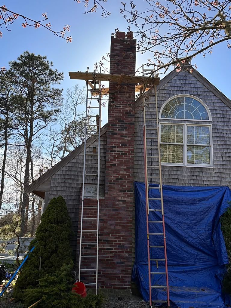 Brick house chimney under repair with ladders and blue tarp covering the wall