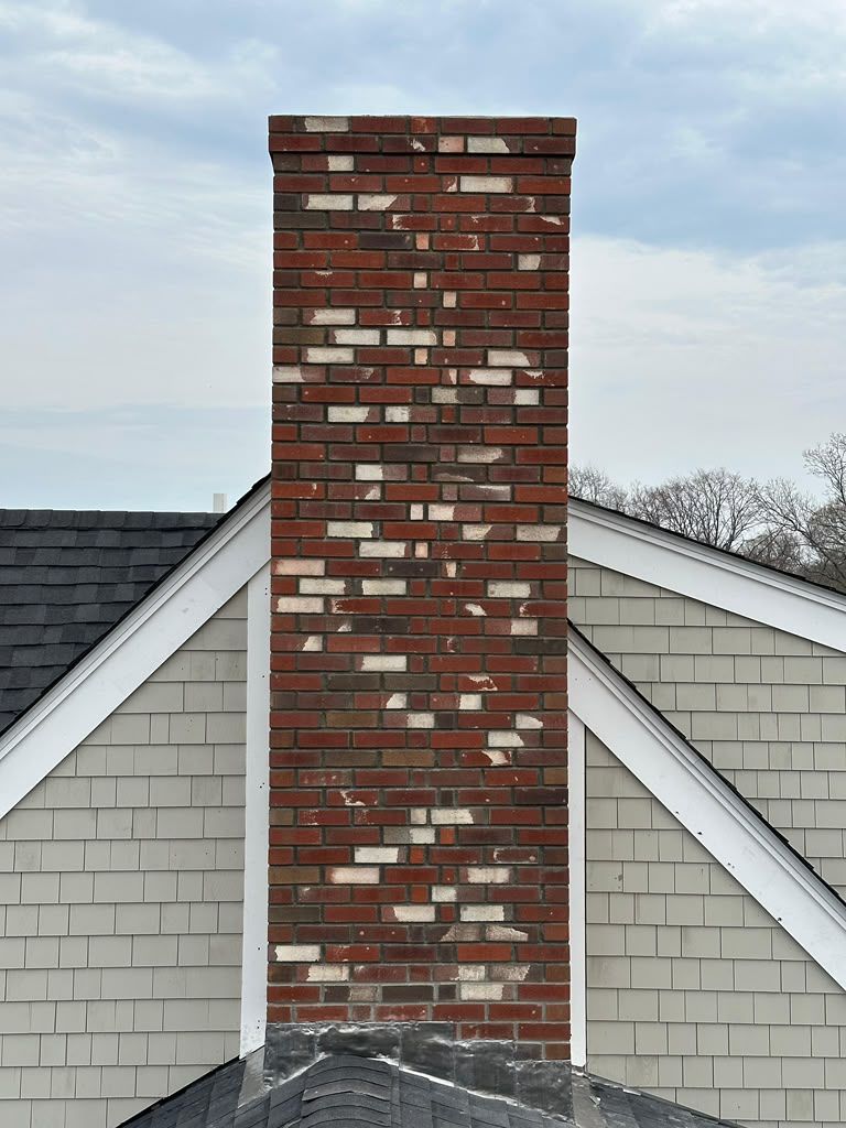 Brick chimney centered on a gray shingled roof against a pale sky.