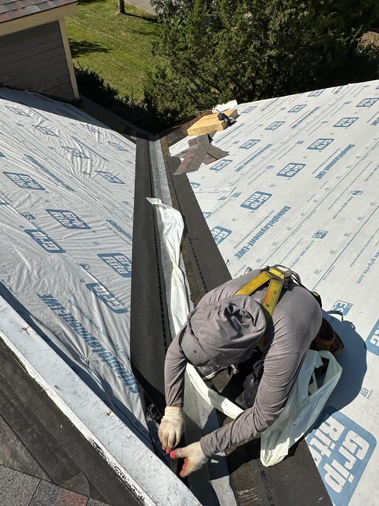 Worker installing roofing membrane on a house roof, crouched near a roof valley.