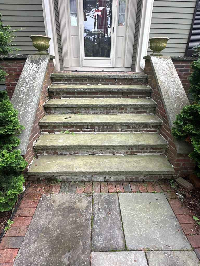 Front steps of a house with worn stone stairs, brick sides, and a glass front door.