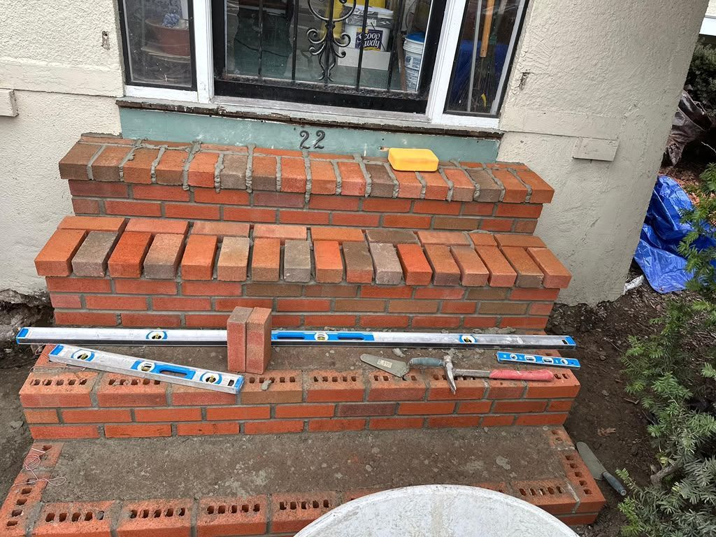 Brick steps with two white measuring sticks, a yellow block, and a house entrance behind them